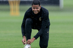 Wesley sorridente amarrando a chuteira no gramado do CT