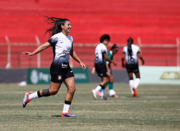 Duda Sampaio celebrando; jogadoras aparecem ao fundo