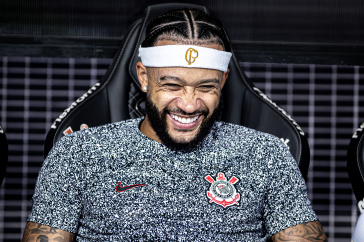 Memphis Depay sorrindo no banco de reservas no jogo contra o Velo Clube