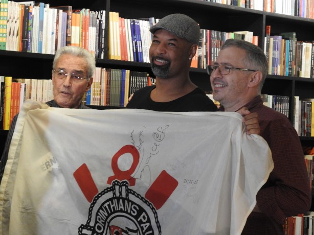 Jos Teixeira e Dinei posam para foto segurando bandeira de 1977, de torcedor corinthiano